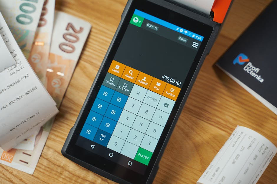 Close-up of a digital payment terminal on a wooden desk with receipts and currency notes.